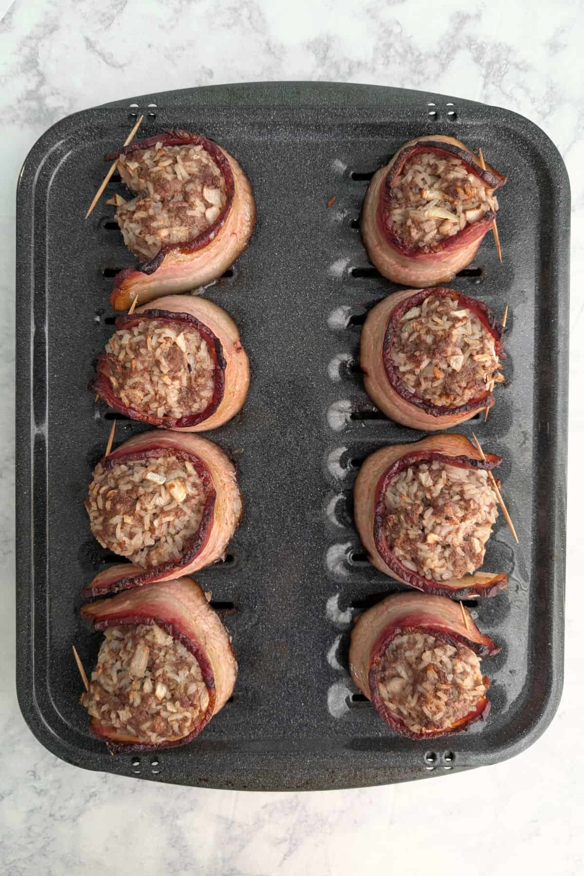 8 fake steak patties wrapped in bacon, on a broiler pan after being baked.