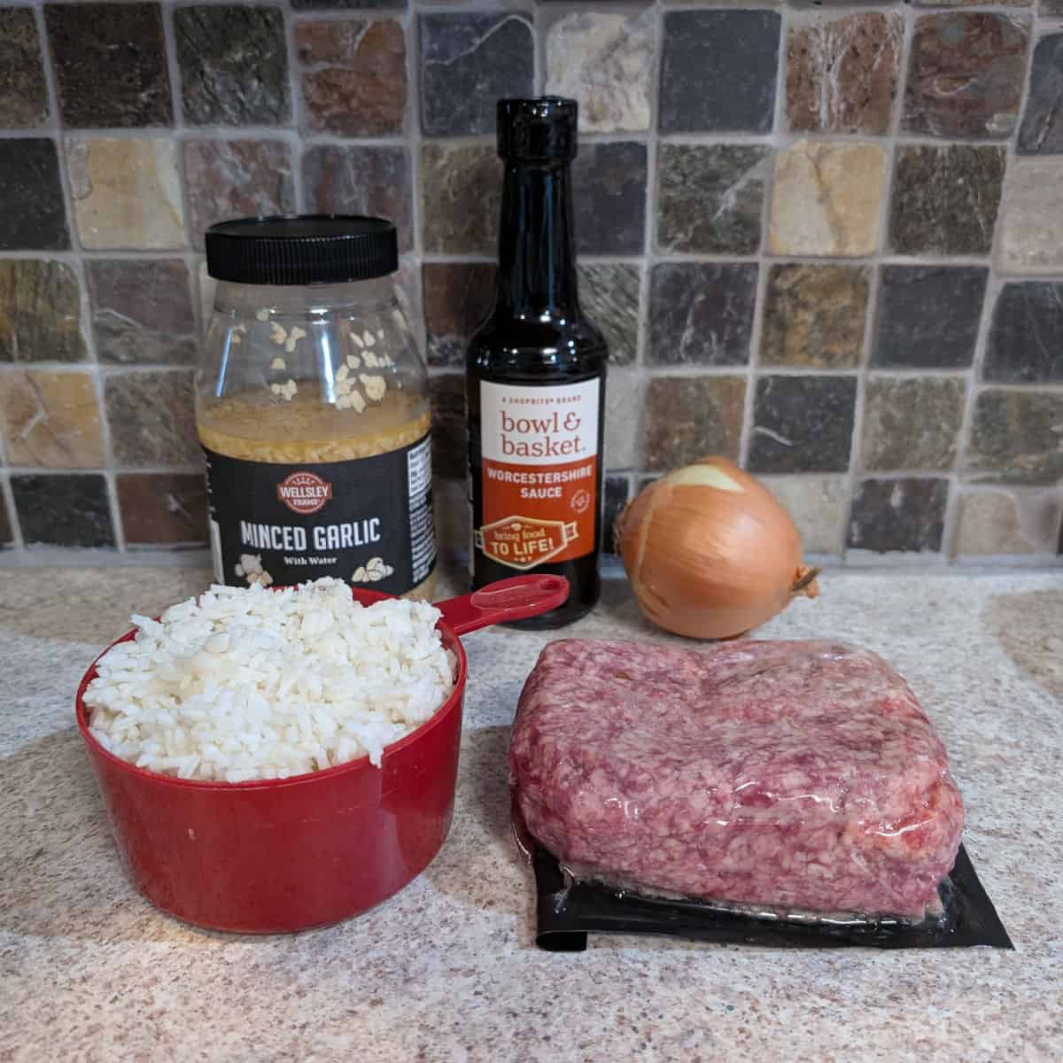 A jar of minced garlic, a bottle of Worcestershire sauce, a whole onion, 2 cups of cooked white rice, and raw ground beef.