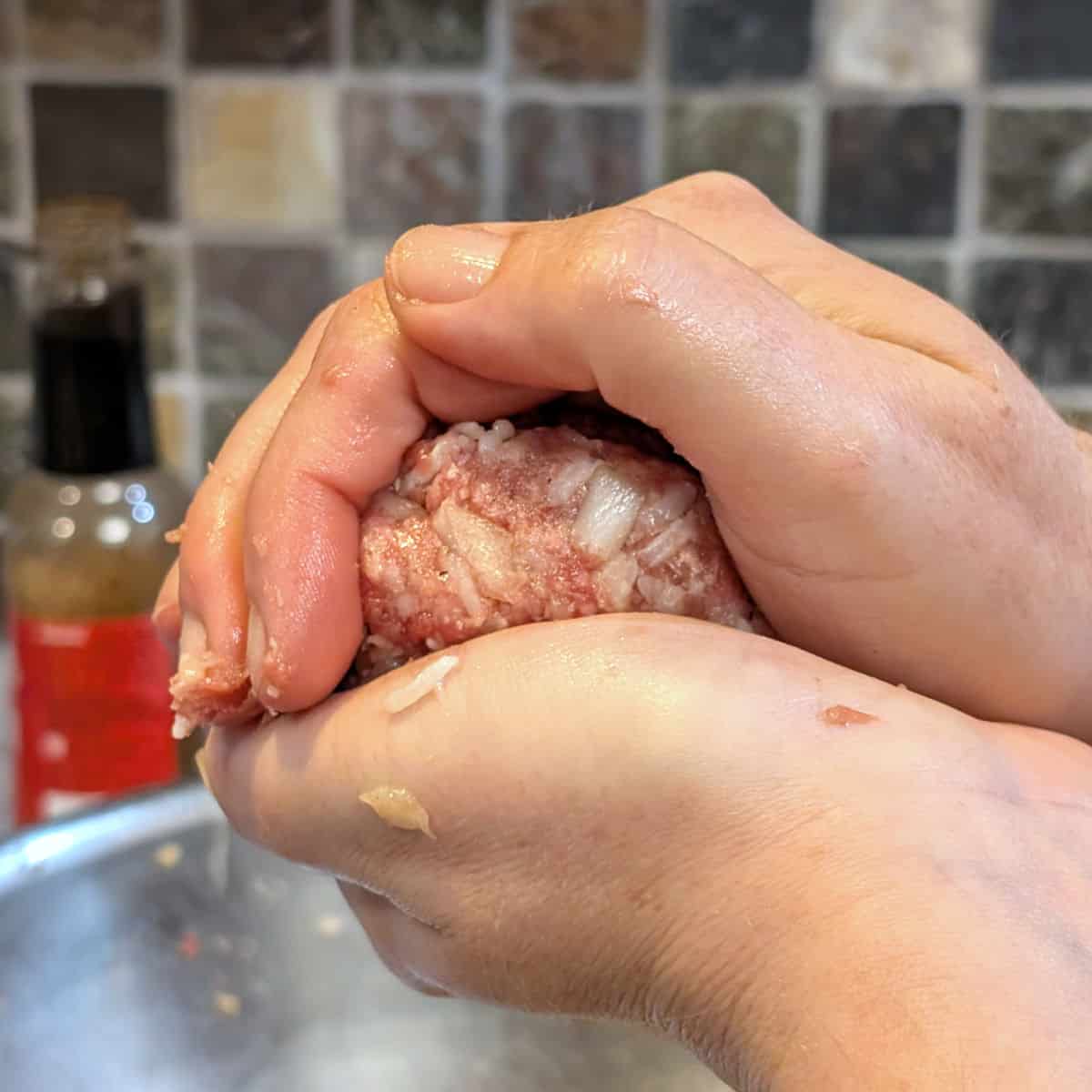 Two hands cupped around a ground beef and rice mixture to shape a patty.