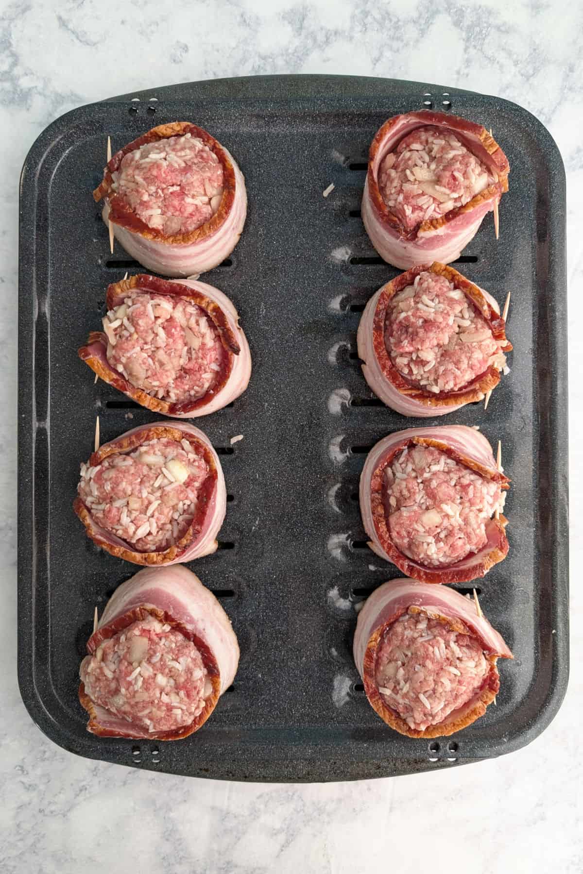 8 fake steak patties with bacon wrapped around them, secured with a toothpick, on a broiler sheet, before being baked.