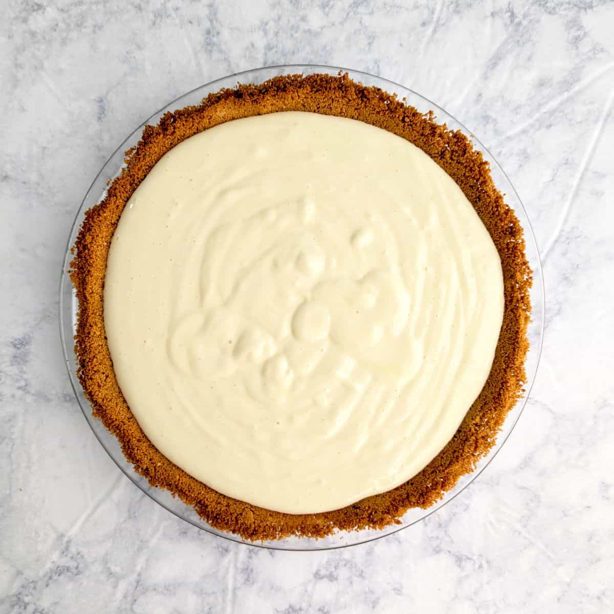 Key lime pie batter in a graham cracker crust in a glass pie plate, before baking.