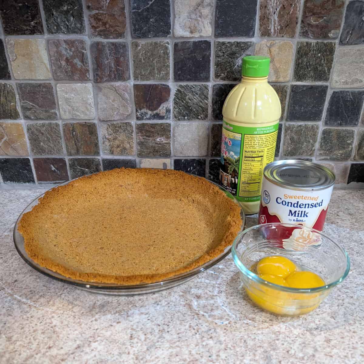 Ingredients for key lime pie: graham cracker crust, bottle of key lime juice, a can of sweetened condensed milk, and 3 egg yolks.