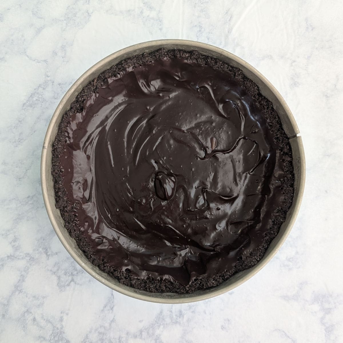 Chocolate ganache spread along the bottom and sides of a chocolate graham cracker crust in a springform pan.