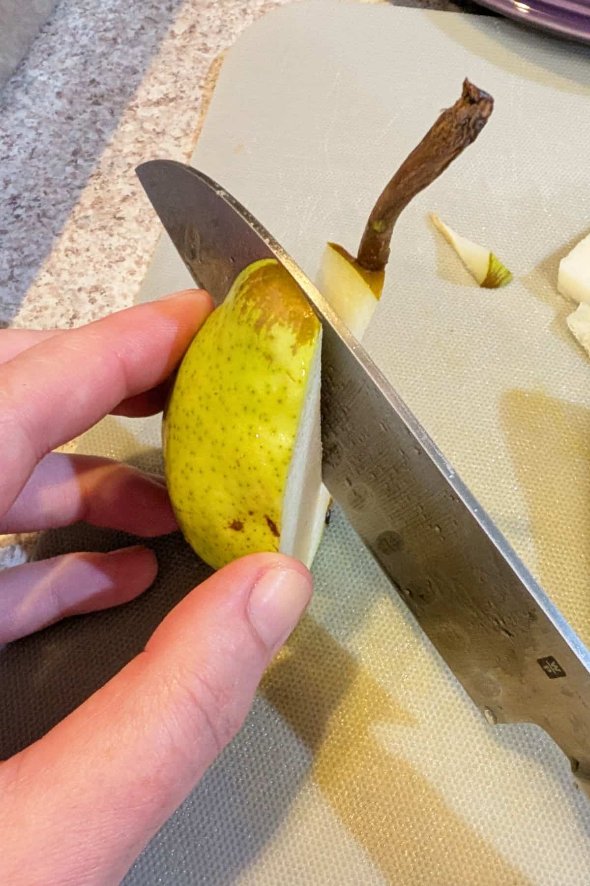 Using a knife to cut the core off of a quarter of a pear.