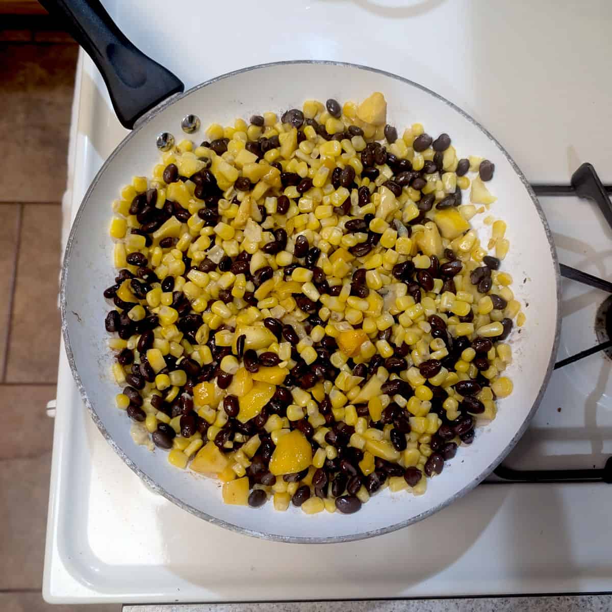 Corn and black beans with chopped mango in a skillet.