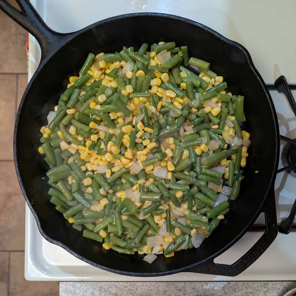 A cast iron skillet with sauteed onion, corn, and green beans.