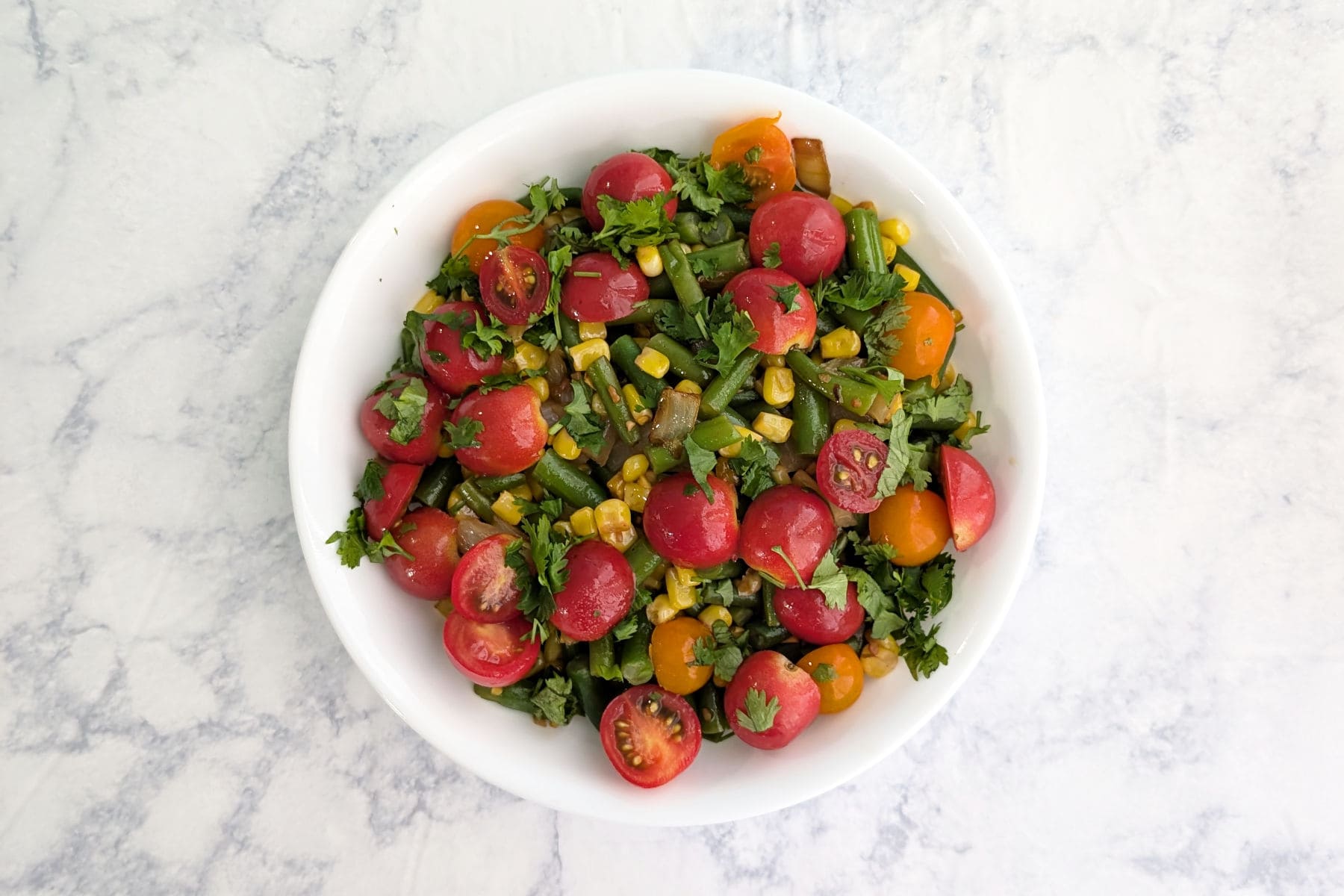 Corn and green bean salad with tomatoes and cilantro on top.