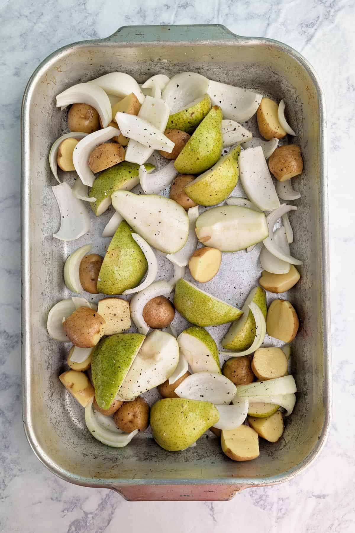 Raw potatoes, pears, and onion slices in a roasting pan.