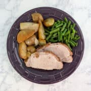 Slices of fennel-crusted pork, with green beans and roasted potatoes, pears, and onions, on a plate.