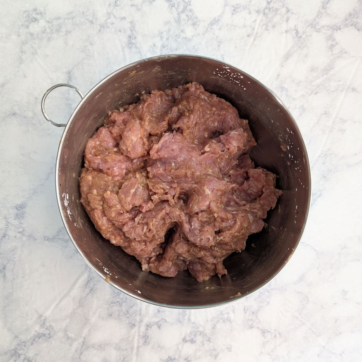 Ground pork mixed with soy sauce, rice wine, and cornstarch, in a metal bowl.
