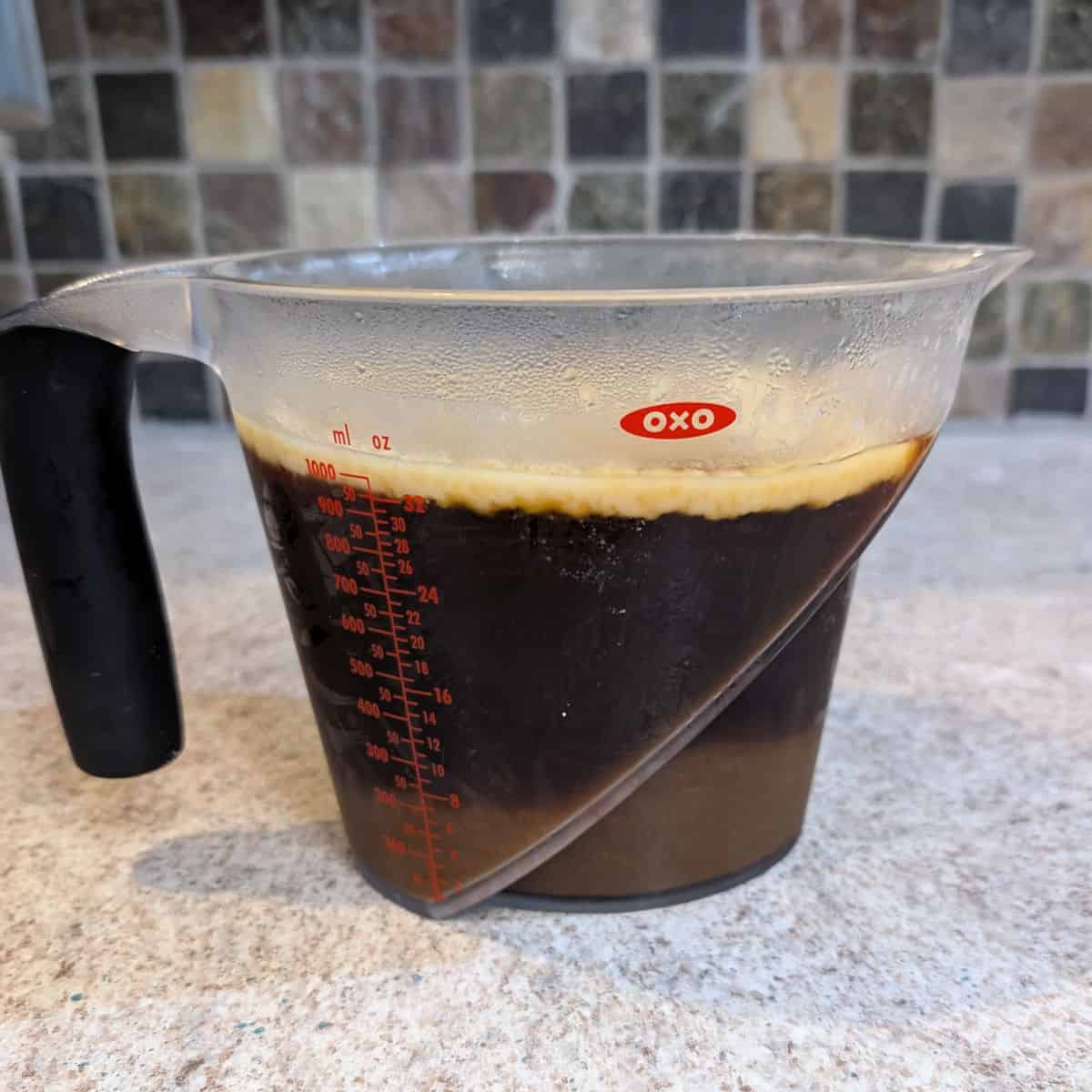 A 4-cup measuring cup containing braising liquid. The fat at the surface has solidified after being refrigerated.