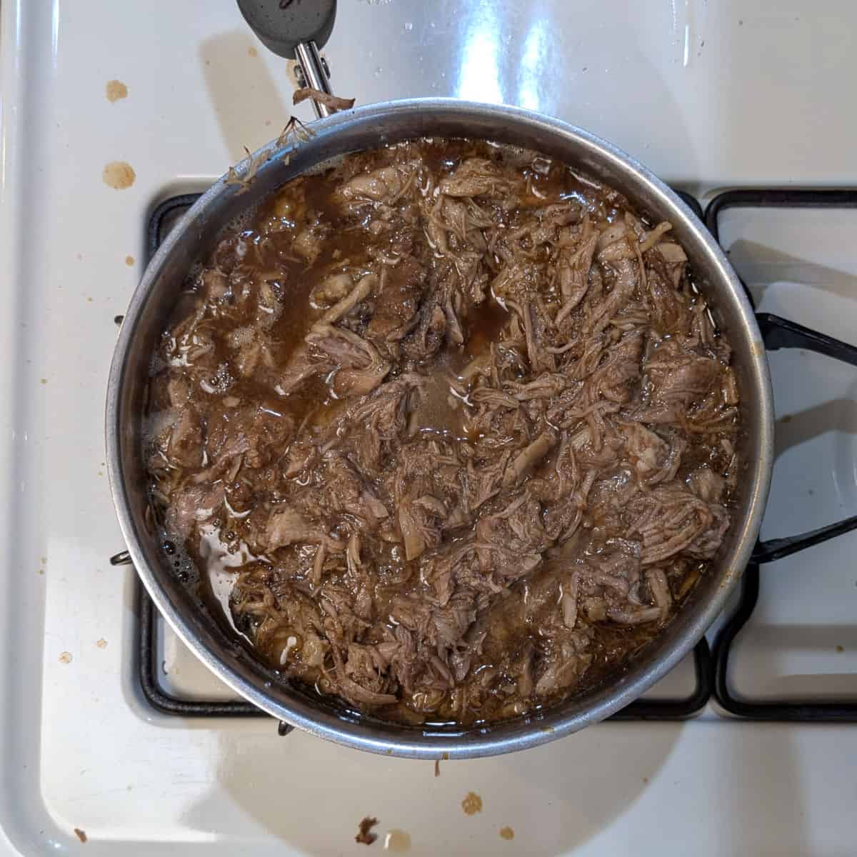 Shredded pork mixed with a reduced soy-cola sauce, in a pot on the stove.