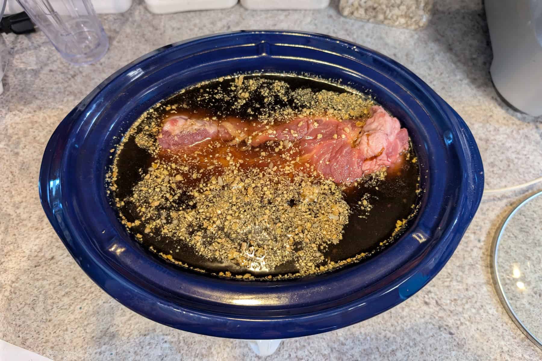 Pork shoulder with soy-cola braising liquid in a slow cooker crock.