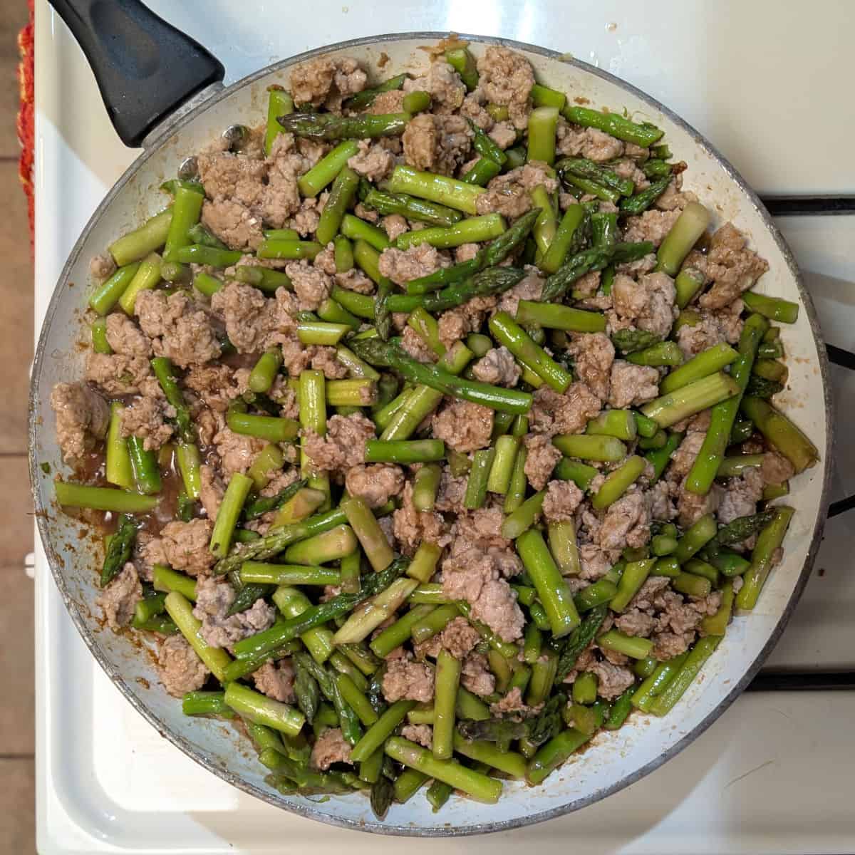 Spicy pork with asparagus, in a skillet on the stove.