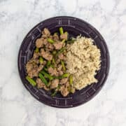 A plate with spicy pork and asparagus plated alongside cooked rice.