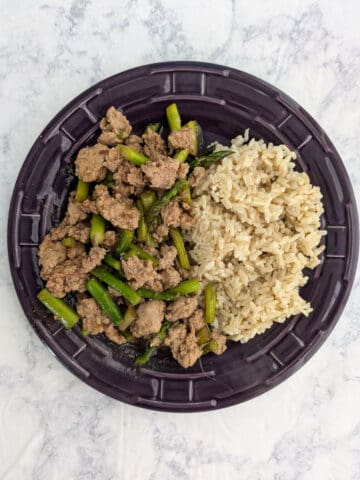 A plate with spicy pork and asparagus plated alongside cooked rice.