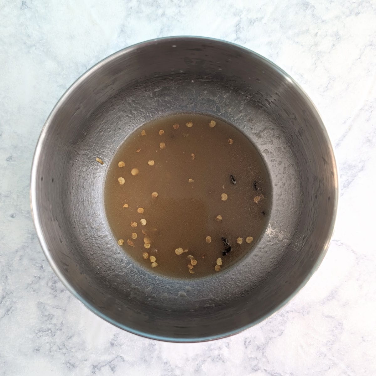A small amount of salad dressing made from lime juice, sesame oil, and jalapeno flakes, in a small metal bowl.