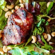 A grilled sirloin steak on a bed of salad greens topped with cashews.