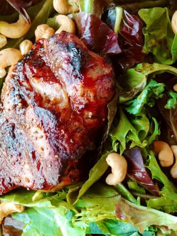 A grilled sirloin steak on a bed of salad greens topped with cashews.