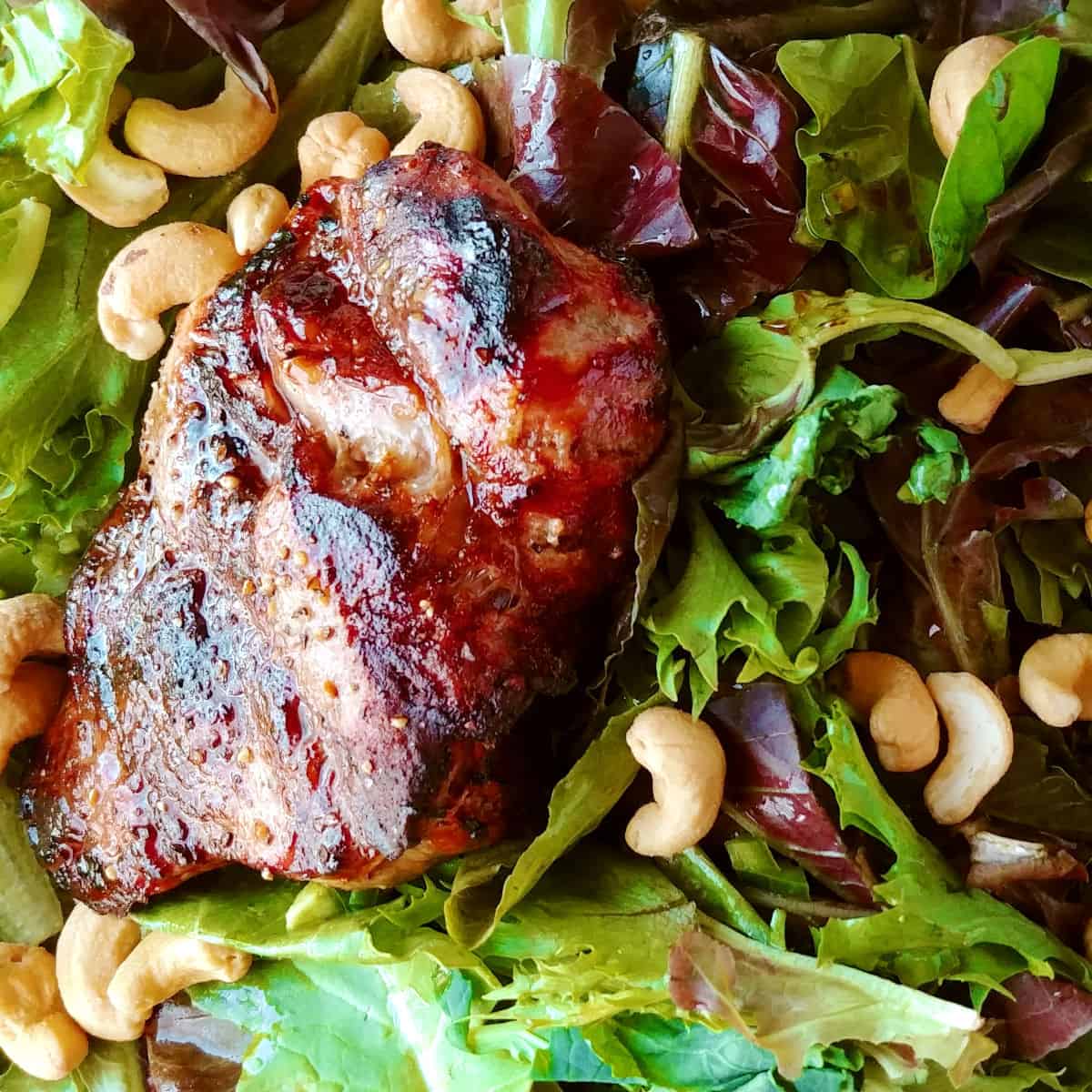 A grilled sirloin steak on a bed of salad greens topped with cashews.