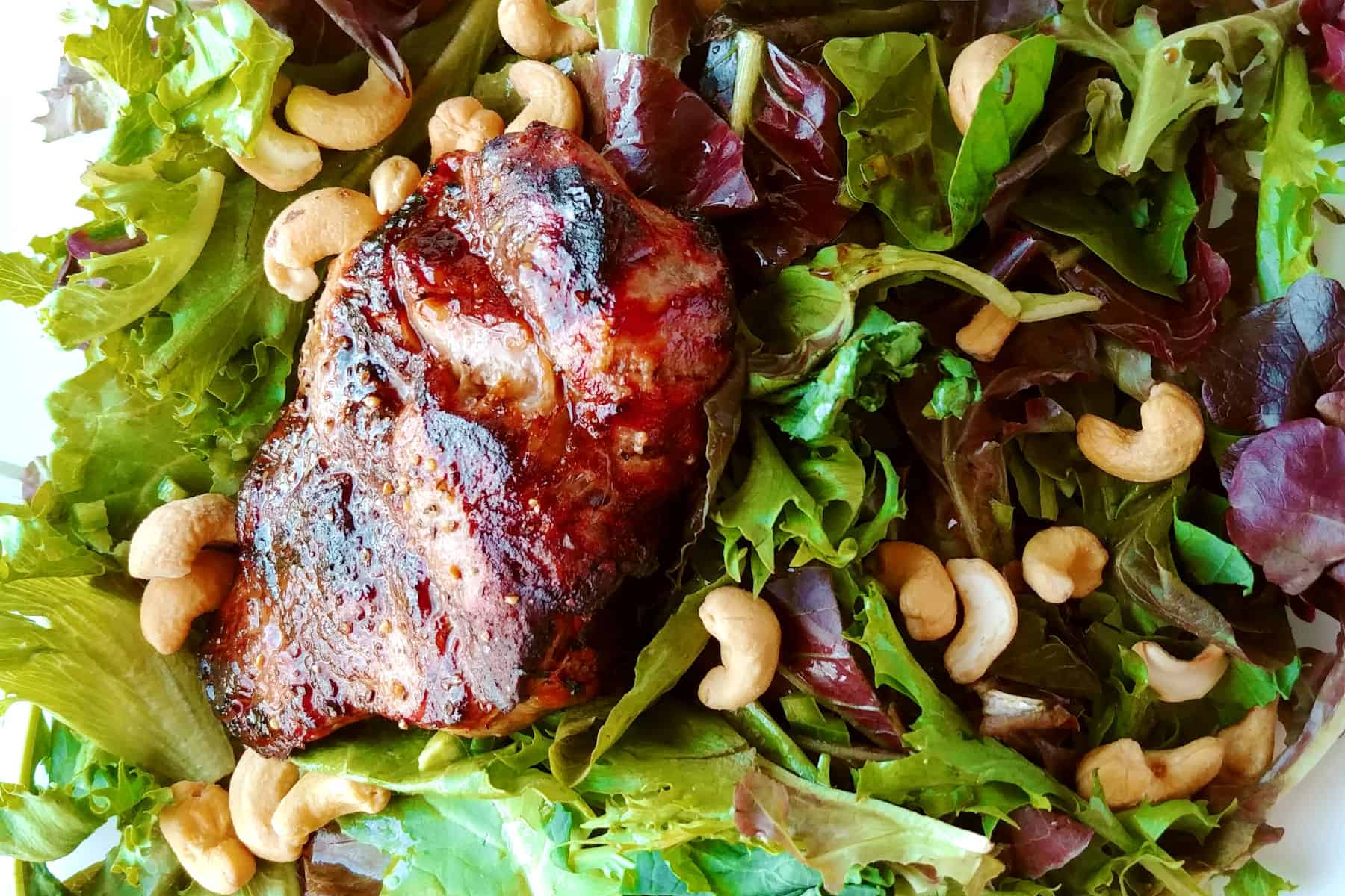A grilled sirloin steak on a bed of salad greens topped with cashews.