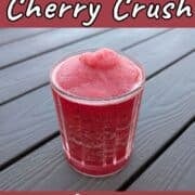 Bourbon cherry crush, a slushy alcoholic drink, in a glass on an outdoor picnic table. Text overlay for Pinterest reads, "Refreshing. Not Too Sweet!"