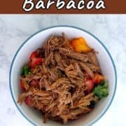 A bowl of shredded barbacoa beef, garnished with peppers and cilantro.