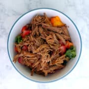 A bowl of shredded barbacoa beef, garnished with peppers and cilantro.