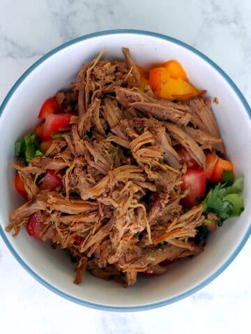 A bowl of shredded barbacoa beef, garnished with peppers and cilantro.