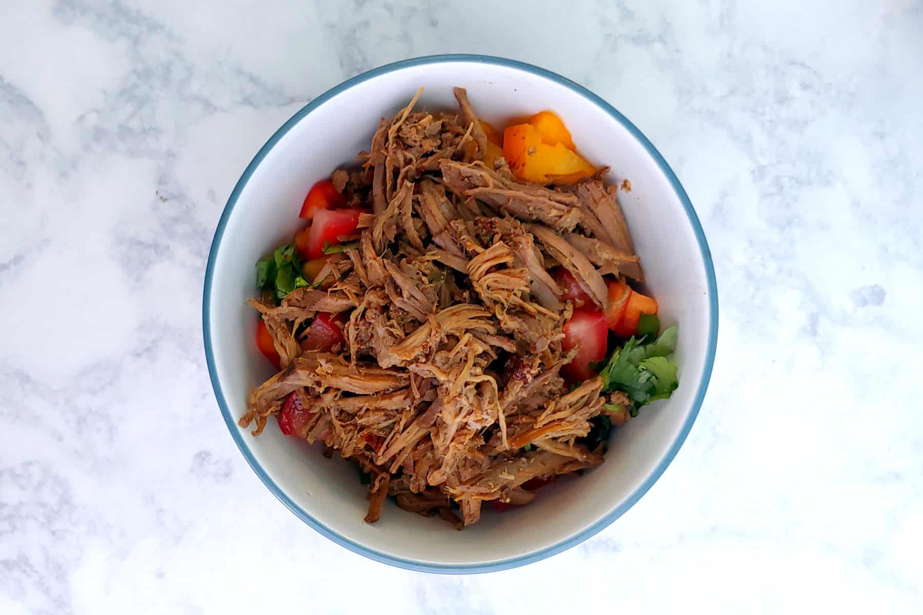 A bowl of shredded barbacoa beef, garnished with peppers and cilantro.
