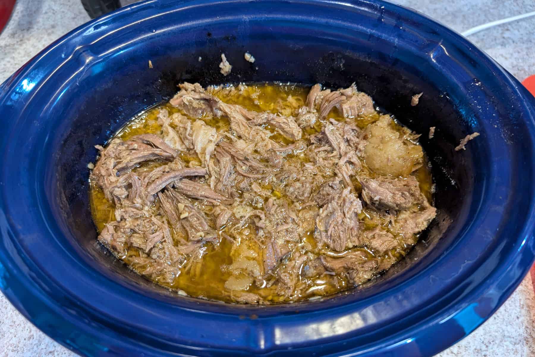 Shredded, cooked barbacoa beef with liquid in a slow cooker crock.