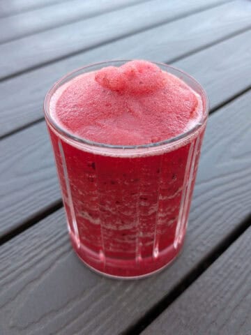 Bourbon cherry crush, a slushy alcoholic drink, in a glass on an outdoor picnic table.