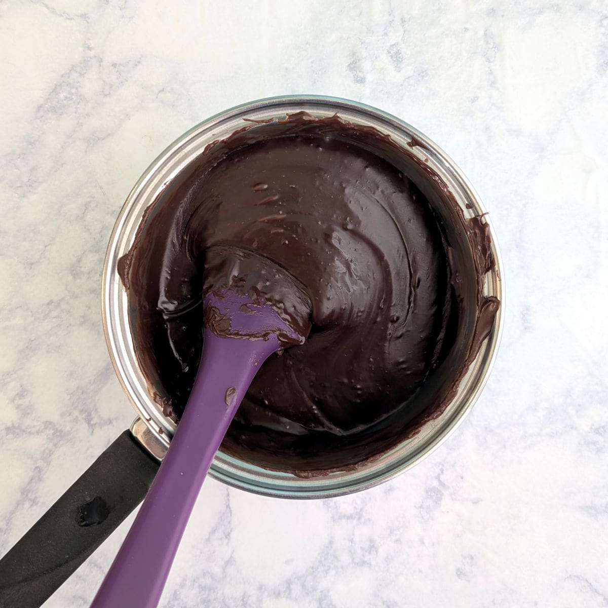 Chocolate fudge in a small saucepan with a rubber spatula.