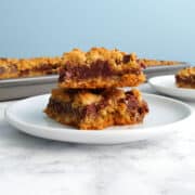A stack of two chocolate oat bars on a plate, in front of a pan.