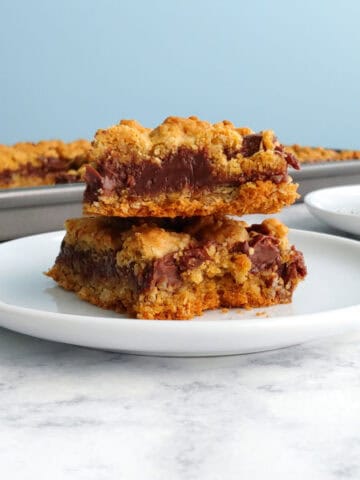 A stack of two chocolate oat bars on a plate, in front of a pan.