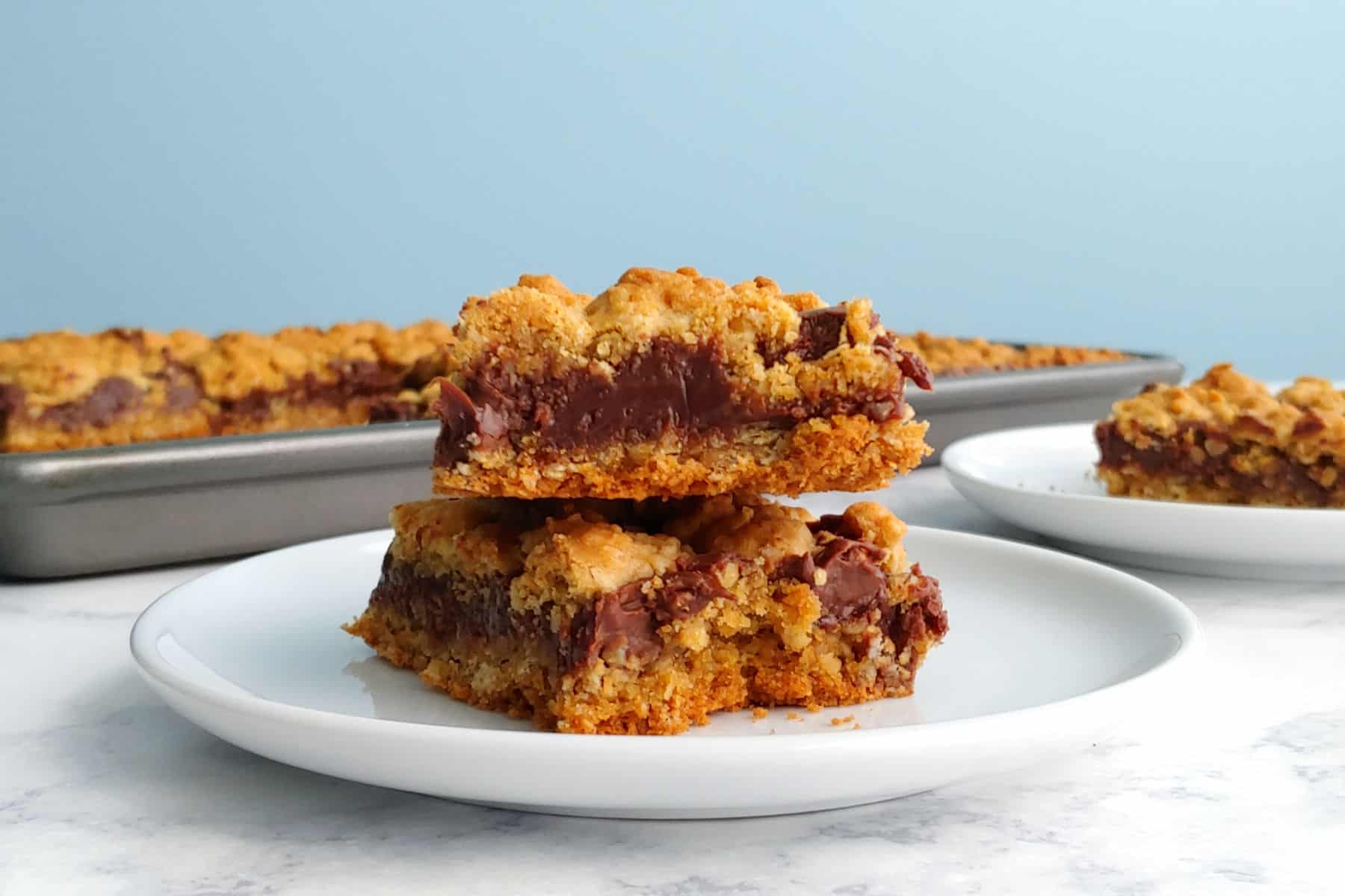 A stack of two chocolate oat bars on a plate, in front of a pan.