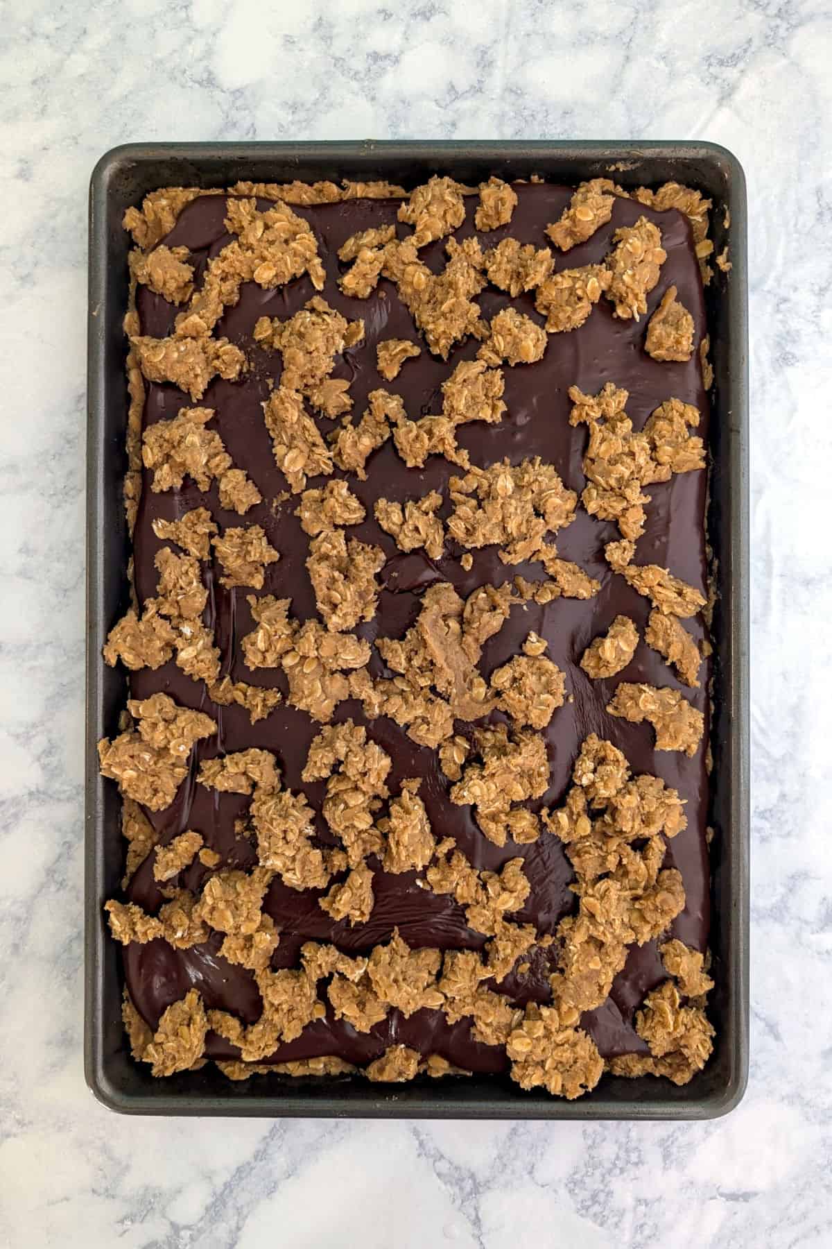 Oatmeal cookie dough layered over chocolate fudge and more oatmeal cookie dough, in a jelly roll pan.