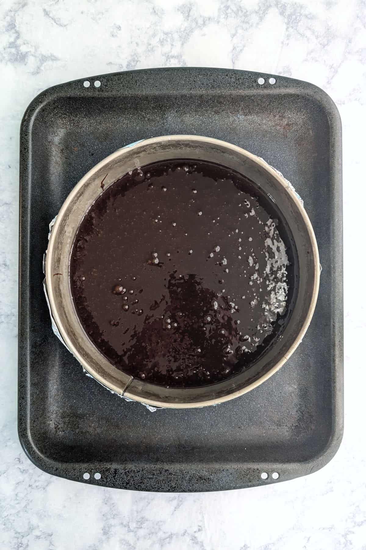 Chocolate truffle cake batter in a Springform pan, wrapped in aluminum foil, in a larger roasting pan.