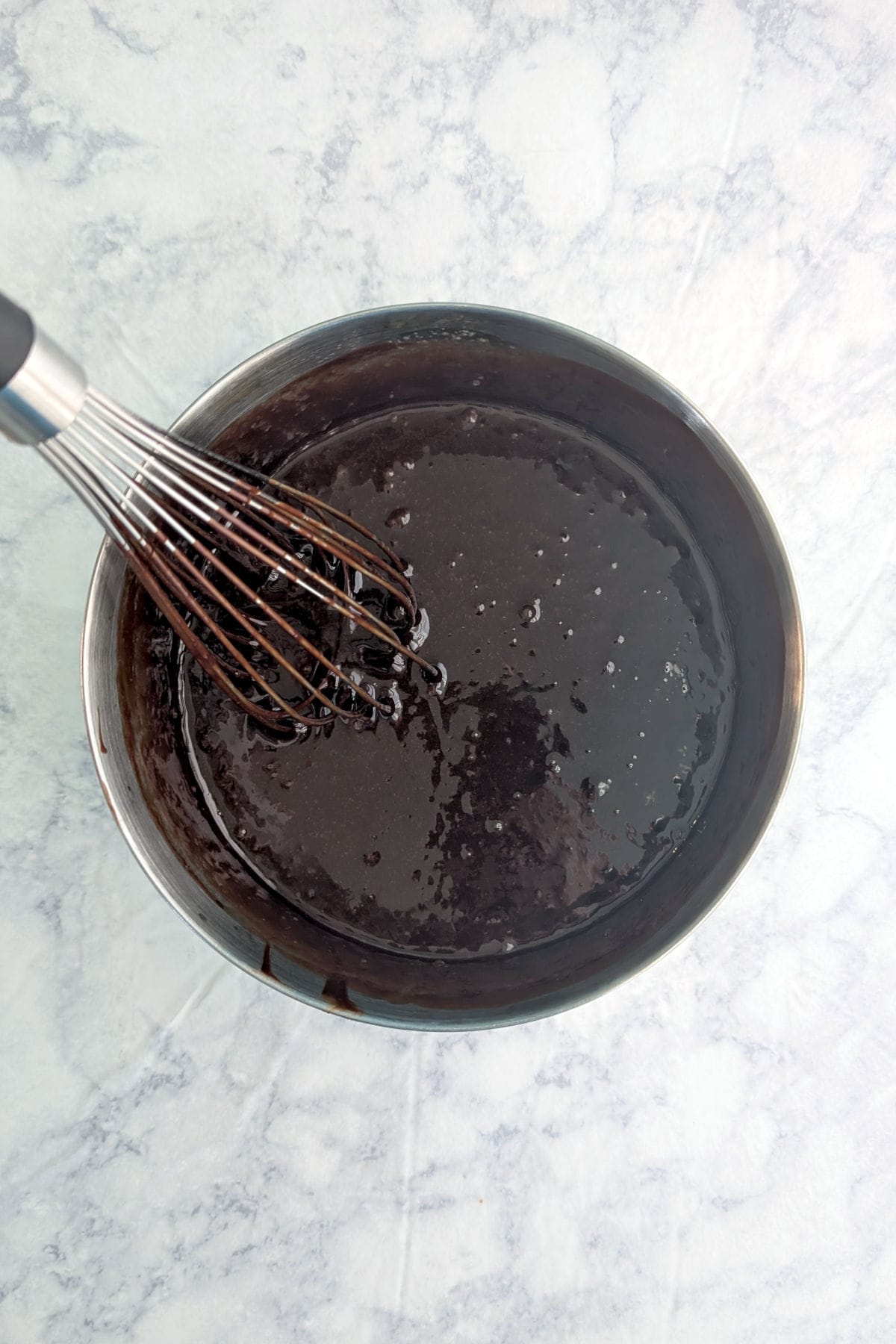 Chocolate truffle cake batter in a metal mixing bowl, with a wire whisk.