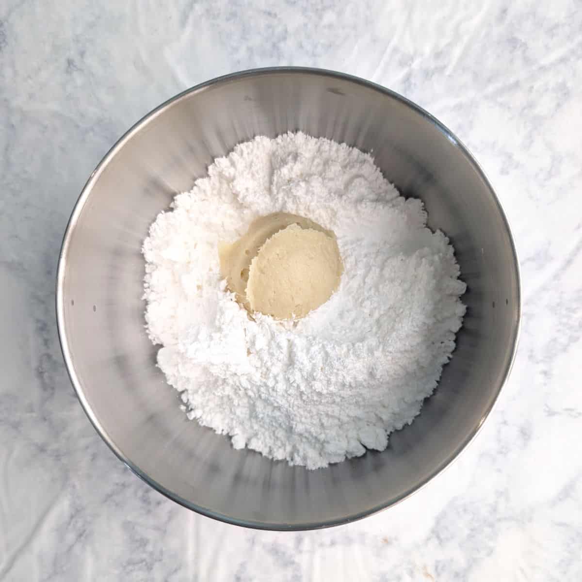 A ball of gooey butter cookie dough, in a bowl of powdered sugar.