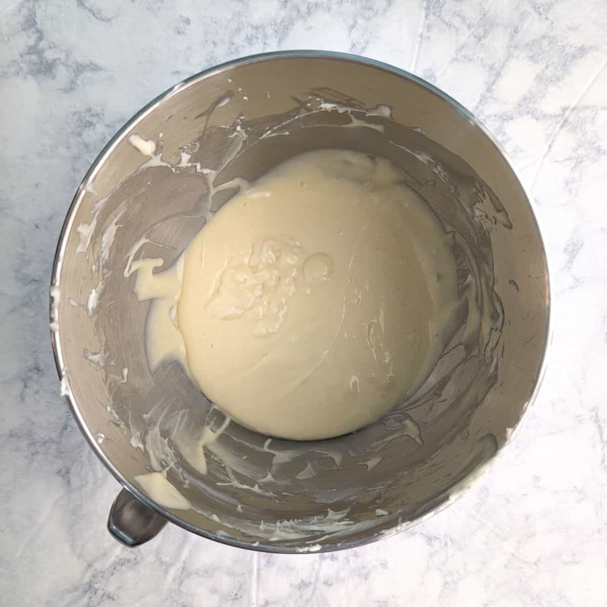 Butter, cream cheese, sugar, vanilla, an egg, and an egg yolk, mixed together in a stand mixer bowl.