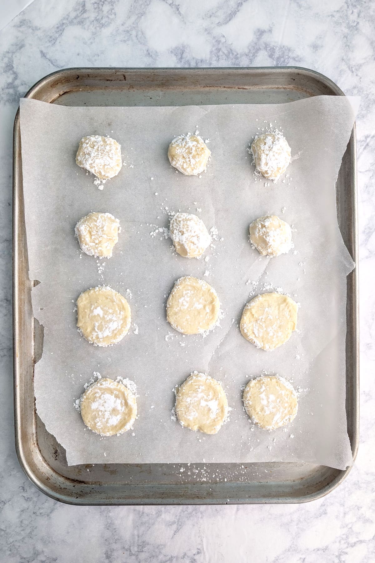 Balls of gooey butter cookie dough, on parchment paper on a baking sheet.