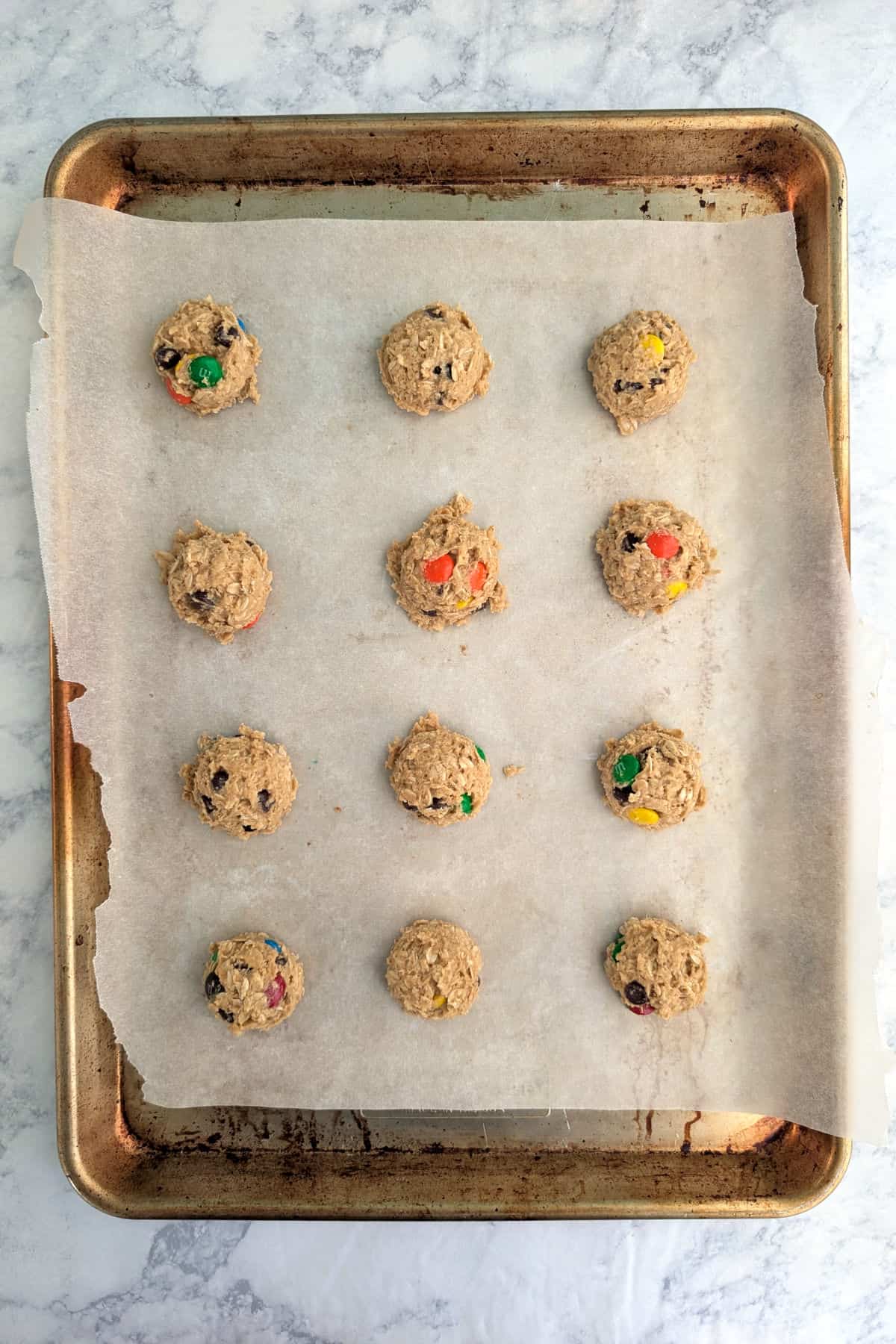 Balls of monster cookie dough, raw, on a baking sheet with parchment paper.