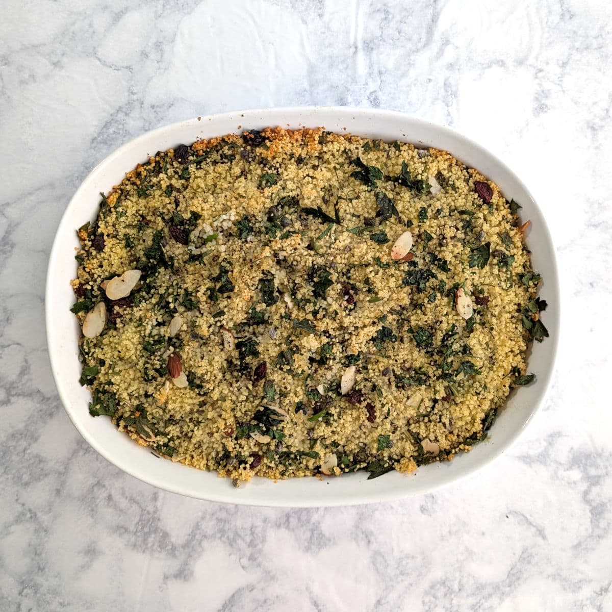Salmon with Baked Couscous and parsley, almonds, raisins, and capers, in a white baking dish.