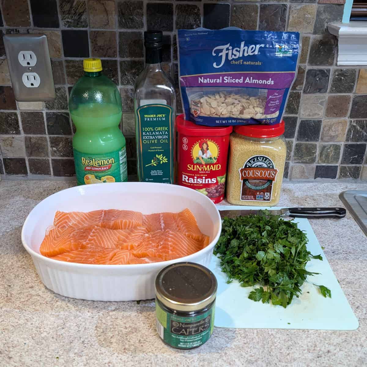 Ingredients for Salmon and Baked Couscous: lemon juice, olive oil, raisins, couscous, almonds, salmon, parsley, and capers.