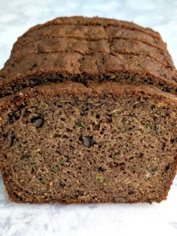 A slice of whole wheat zucchini bread in front of a stack of zucchini bread.