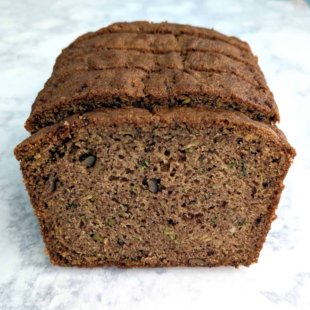 A slice of whole wheat zucchini bread in front of a stack of zucchini bread.