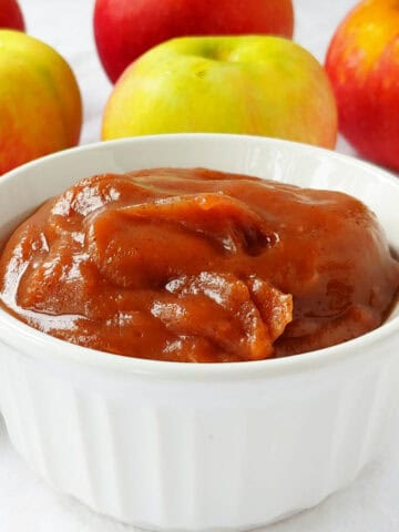 No-sugar-added slow cooker apple butter in a ramekin, in front of apples.