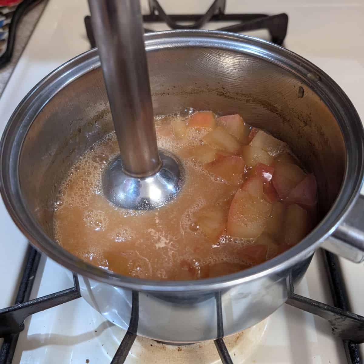 Cooked apples and apple cider, in a pot, being blended with an immersion blender.
