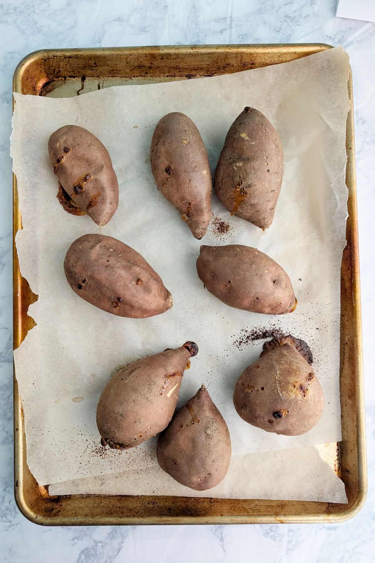 Whole baked sweet potatoes, on a baking sheet lined with parchment paper.